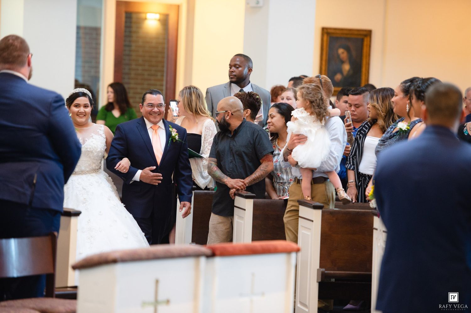 Bride and groom walk down the aisle surrounded by smiling wedding guests inside a church ceremony.