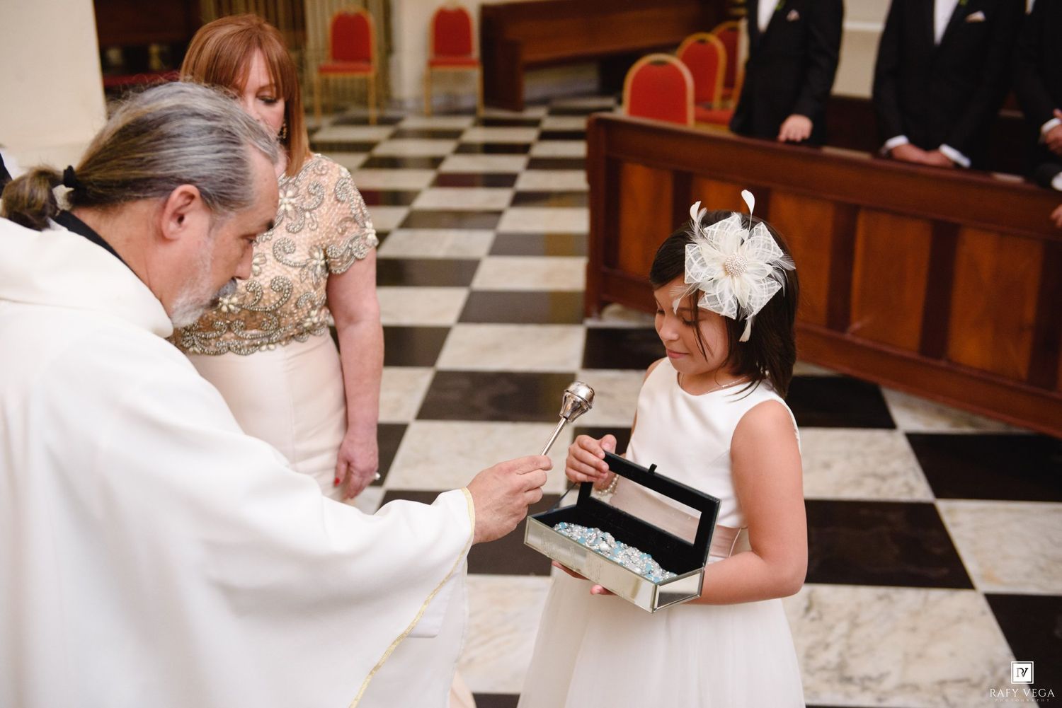 Young flower girl presents wedding rings to priest during elegant church wedding ceremony.
