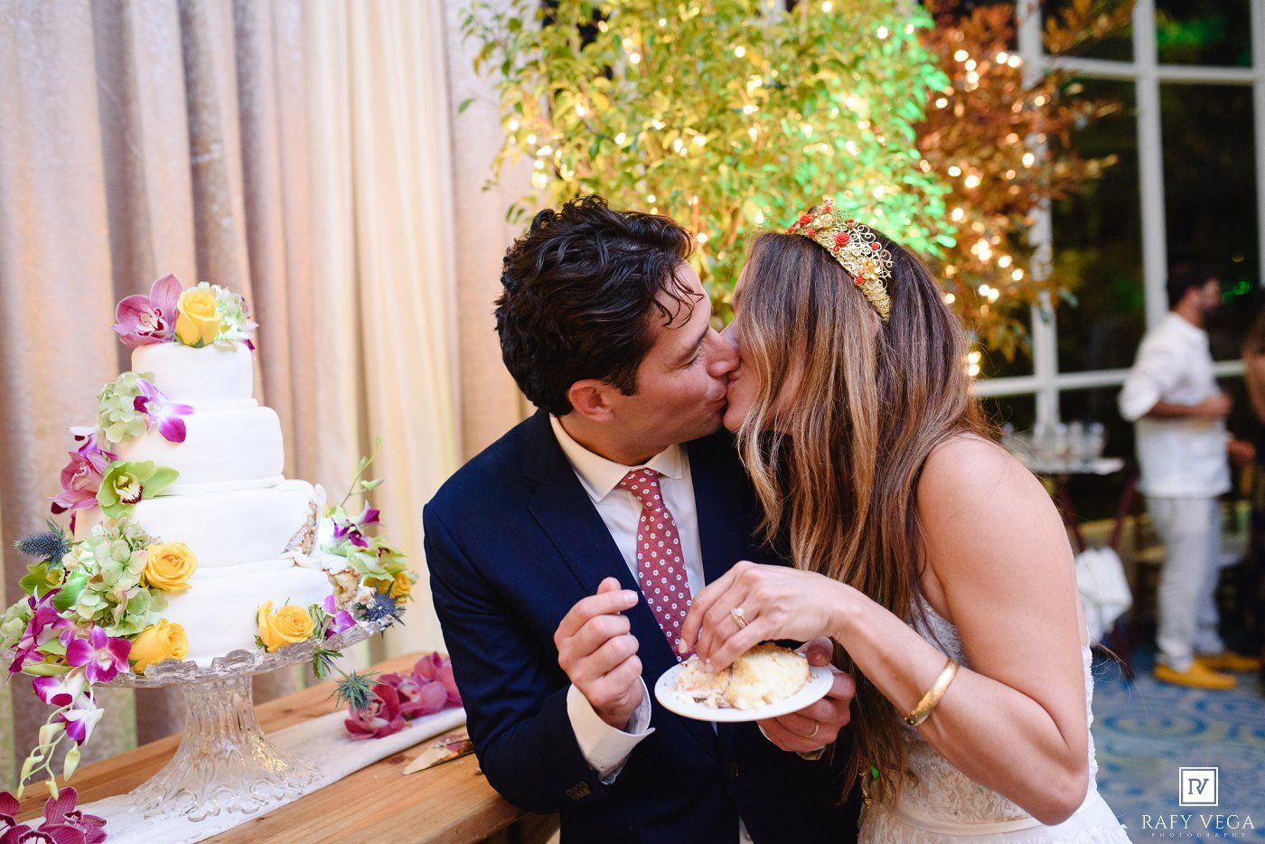 Newlyweds share a kiss while cutting their colorful floral wedding cake.