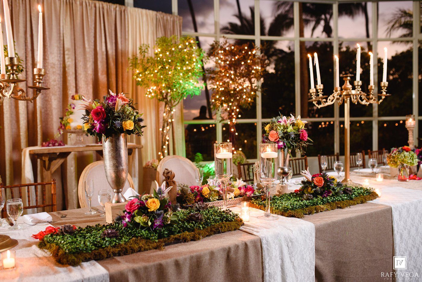 Elegant wedding reception table adorned with lush greenery, colorful floral arrangements, candelabras, and warm fairy lights.