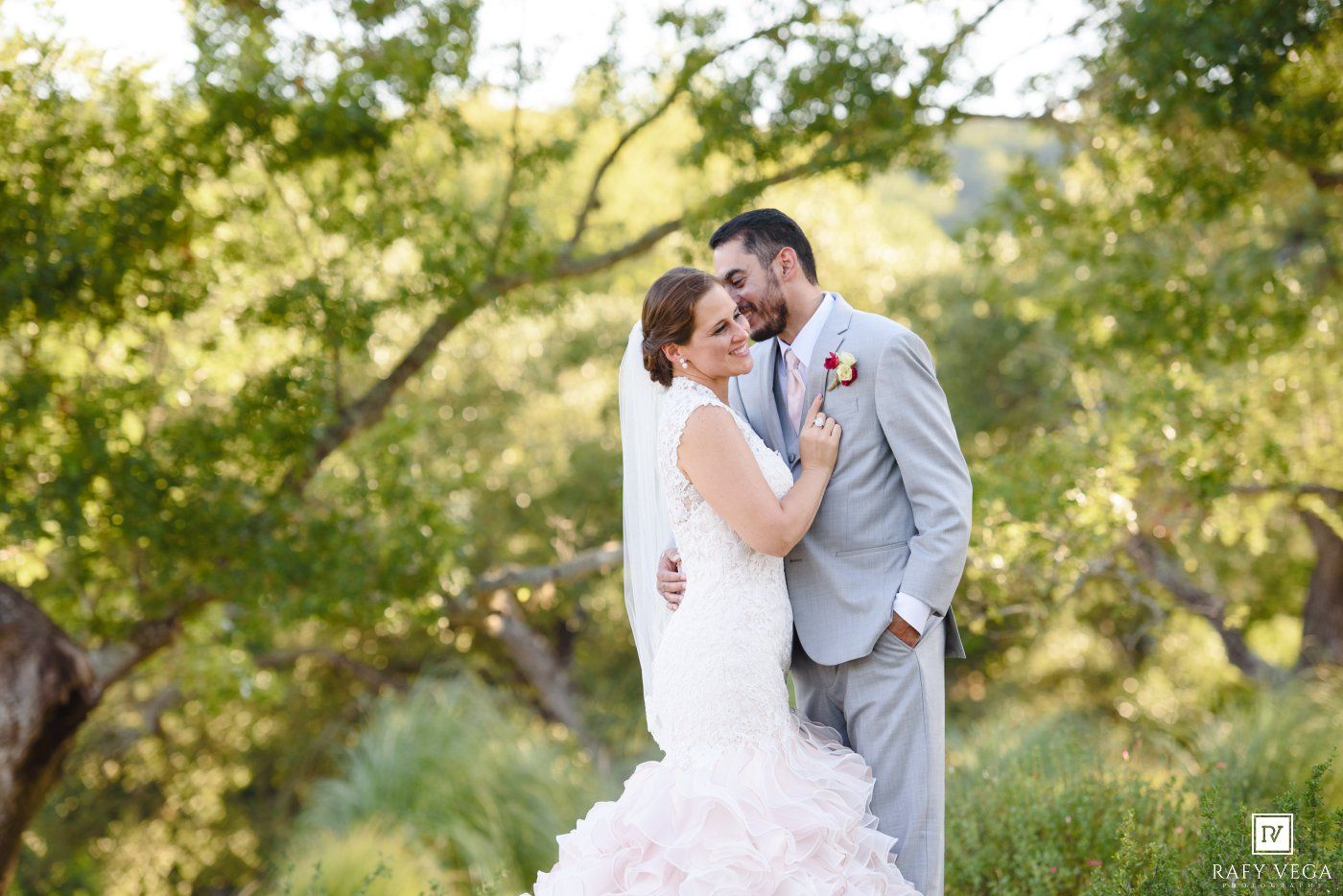 Bride and groom share a romantic moment outdoors surrounded by lush green trees on their wedding day.