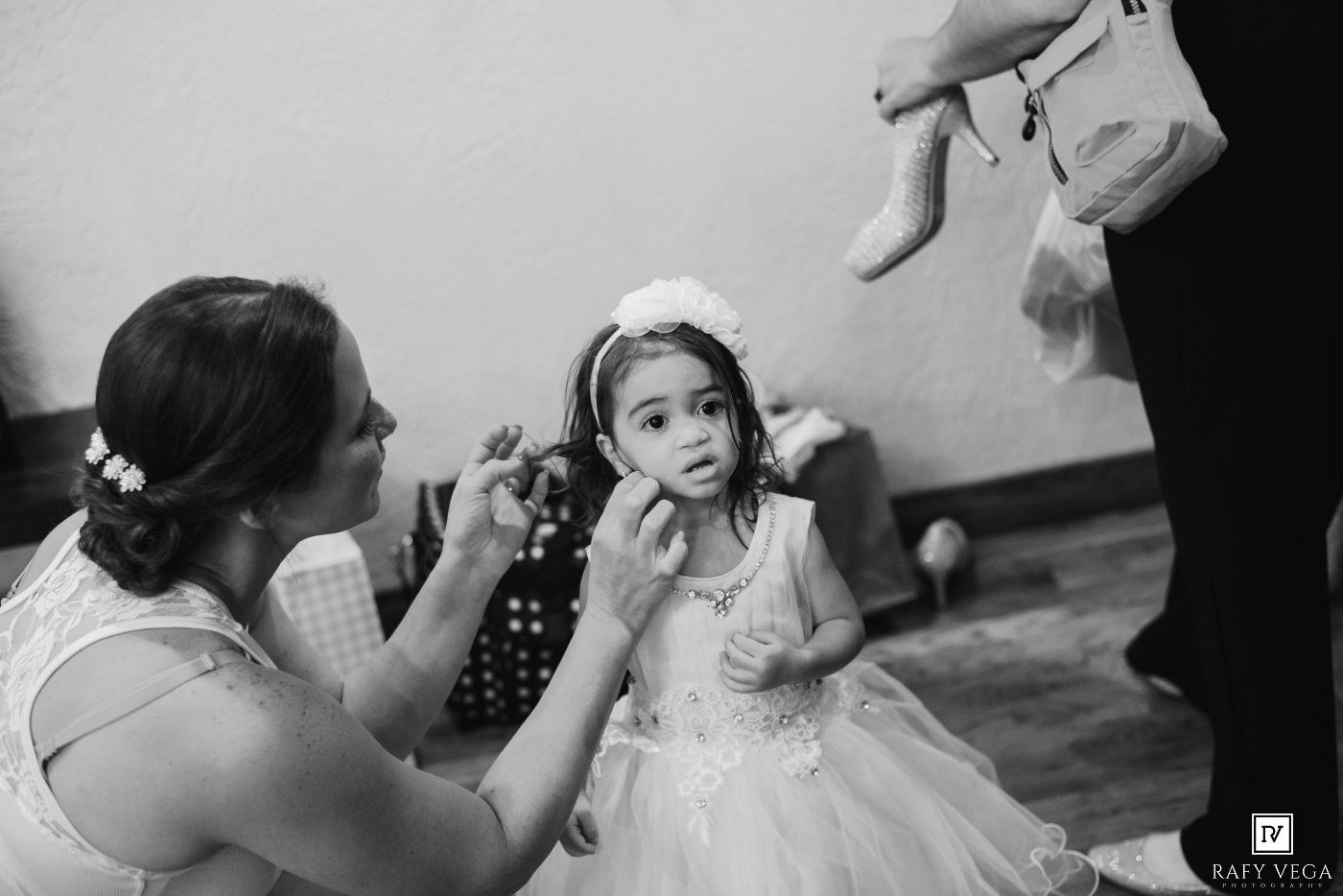 Black and white photo of a woman adjusting a flower girl's hair accessory at a wedding ceremony.