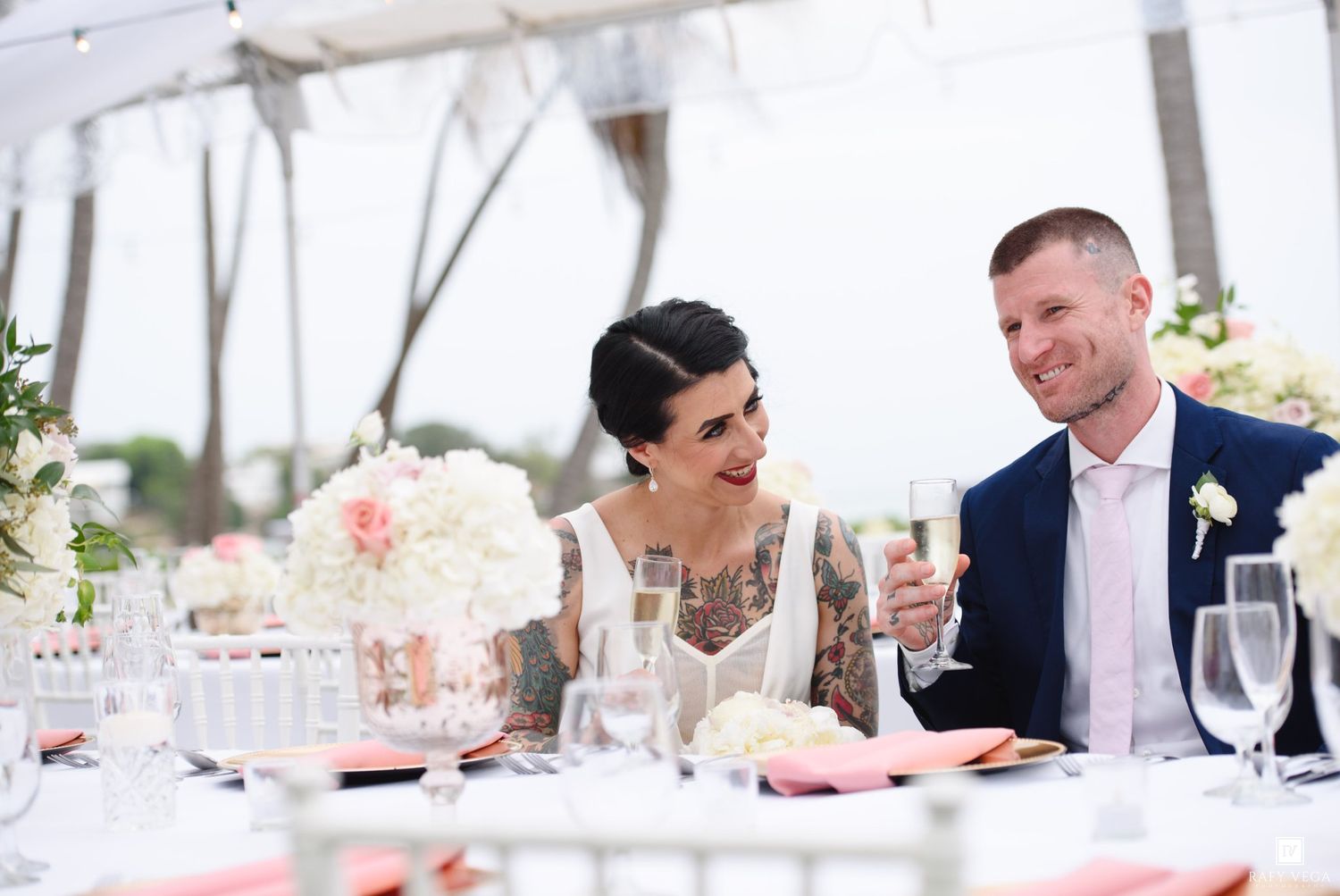 A bride and groom share a joyful moment at their elegant outdoor wedding reception, toasting with champagne flutes.