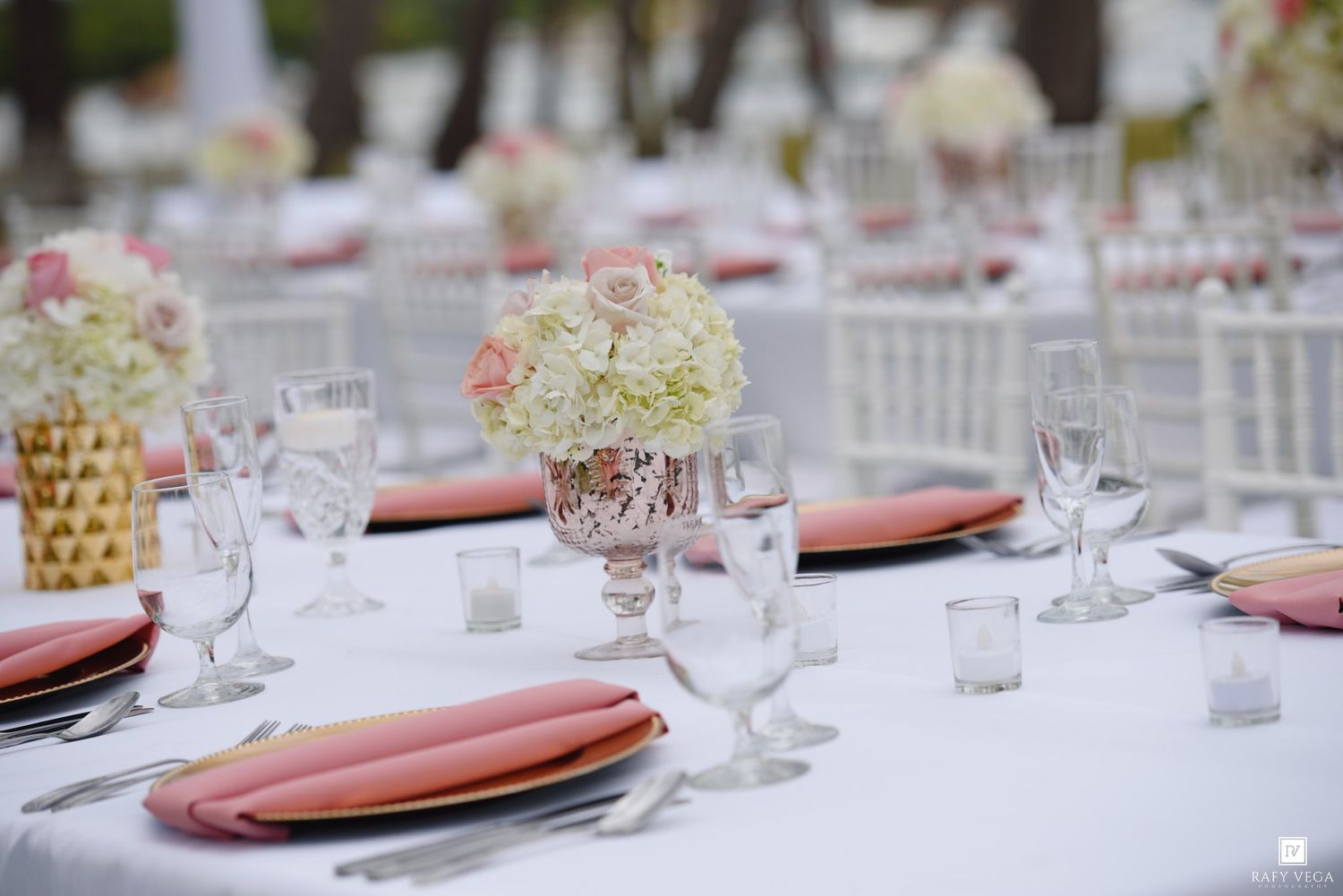 Elegant wedding reception table with pink napkins, crystal glasses, and floral centerpieces on a white tablecloth.