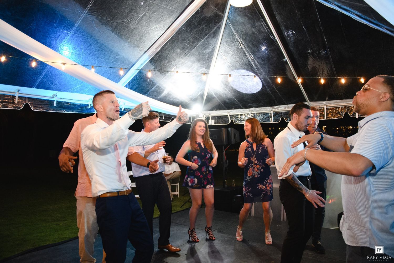 Guests dancing and celebrating under a tent with string lights at a lively outdoor evening party event.