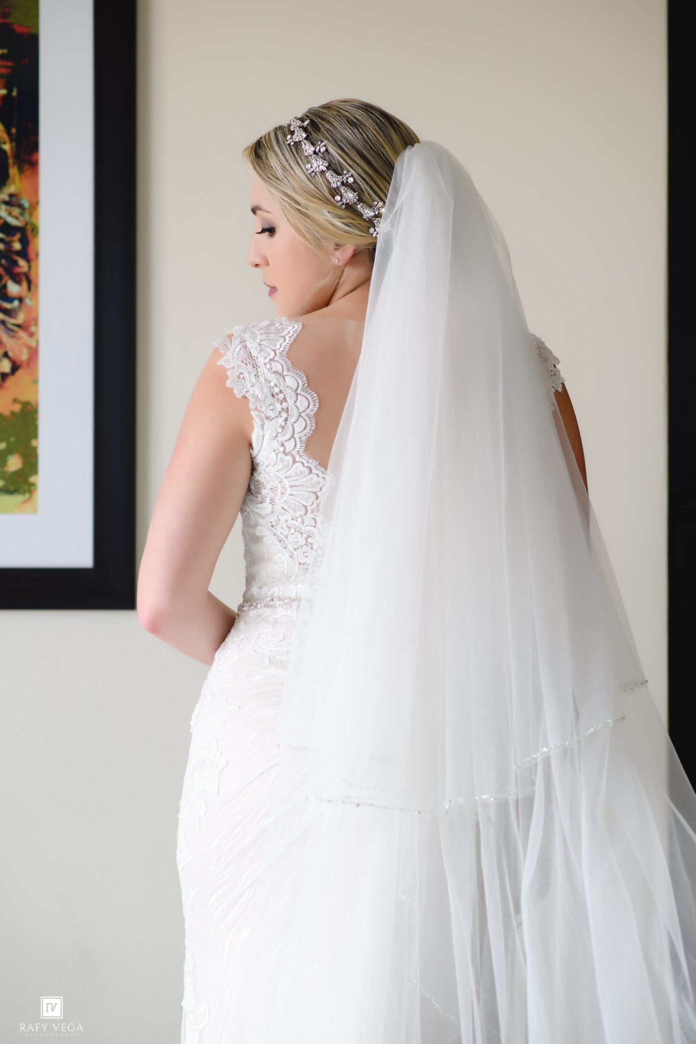 Bride in white lace wedding dress and tiered veil with crystal headpiece, posed elegantly in profile view.