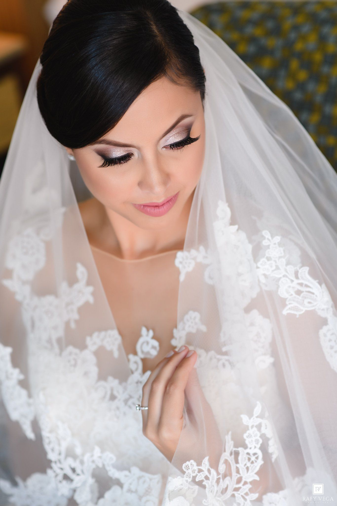 Elegant bride in lace wedding dress and veil, wearing natural glam makeup, looking down at her ring.