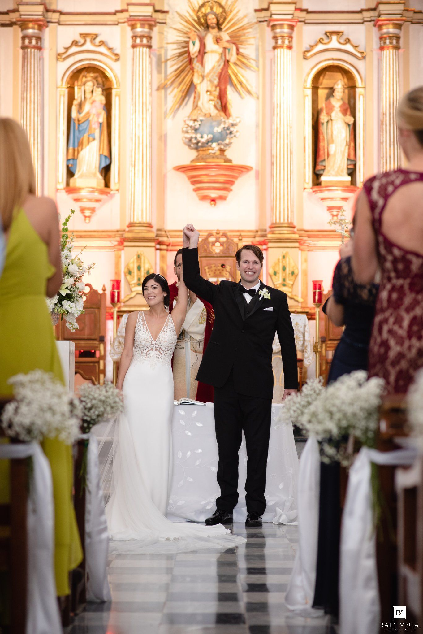 Bride and groom celebrate at church altar after wedding ceremony, groom raising fist in joy.