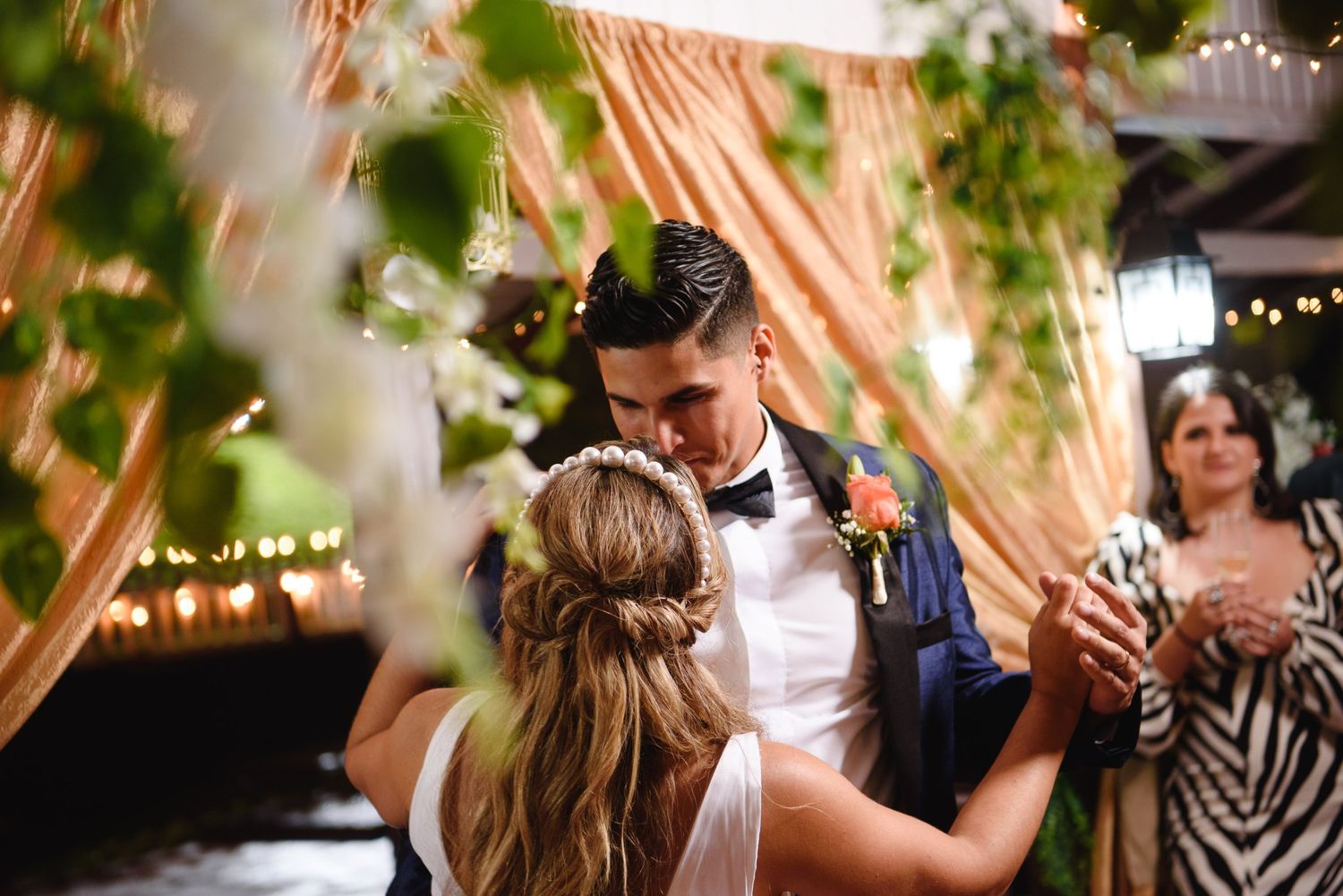Bride and groom share their first dance surrounded by greenery and warm fairy lights at a romantic wedding reception.