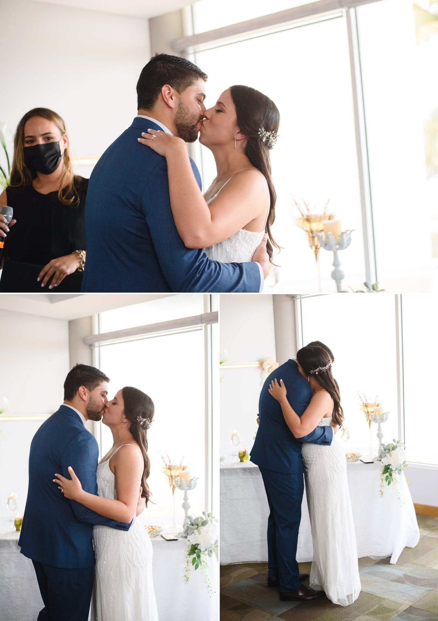 Bride and groom share their first kiss at wedding ceremony, officiant in black mask nearby, bright window backdrop.