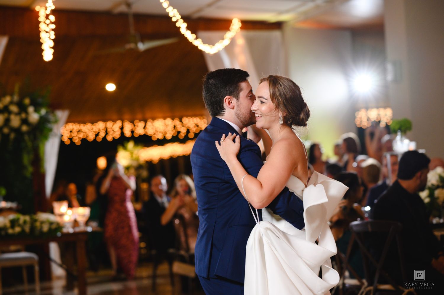 Bride and groom share their first dance at elegant wedding reception with string lights and floral decor.