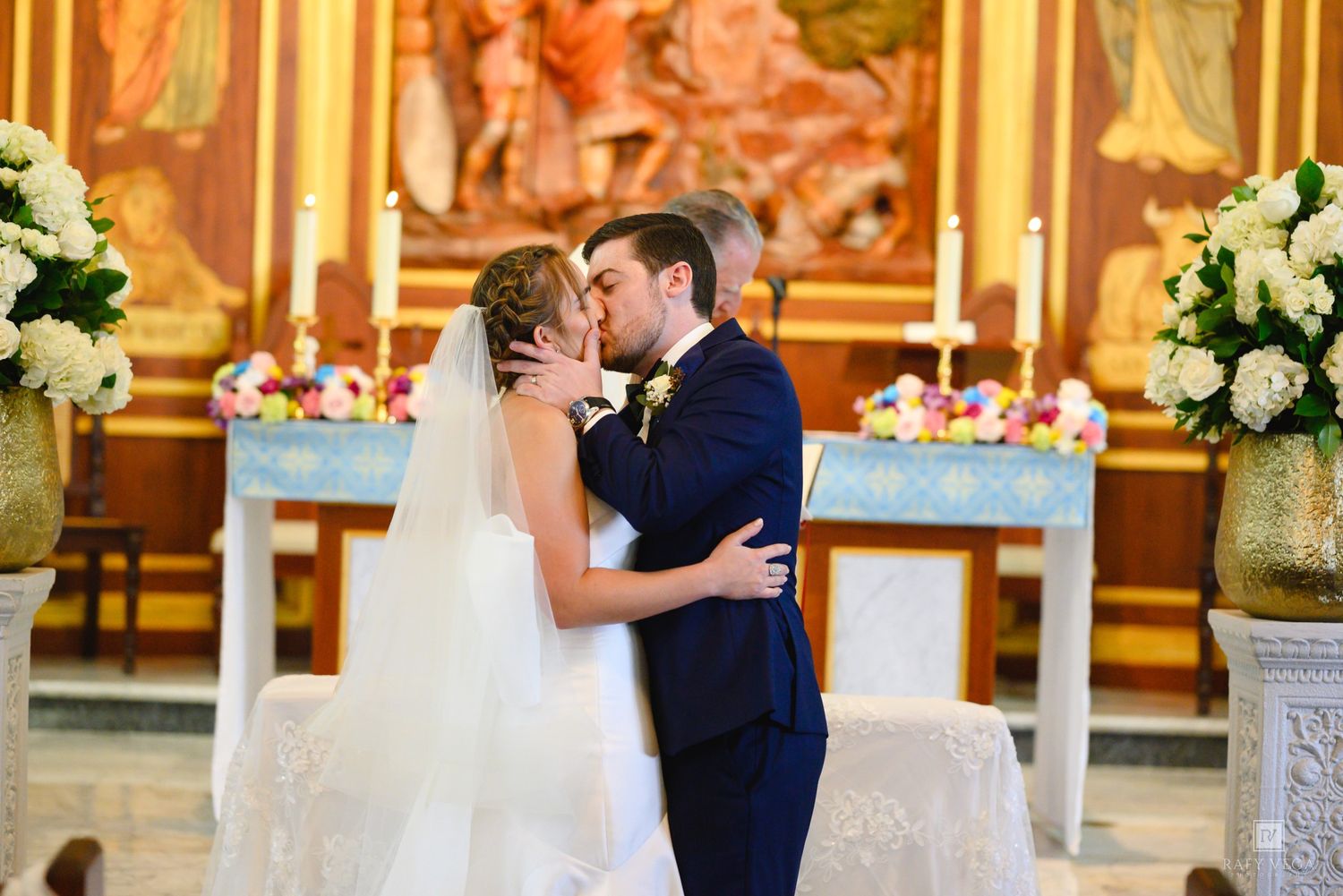Bride and groom share first kiss at ornate church altar during wedding ceremony.