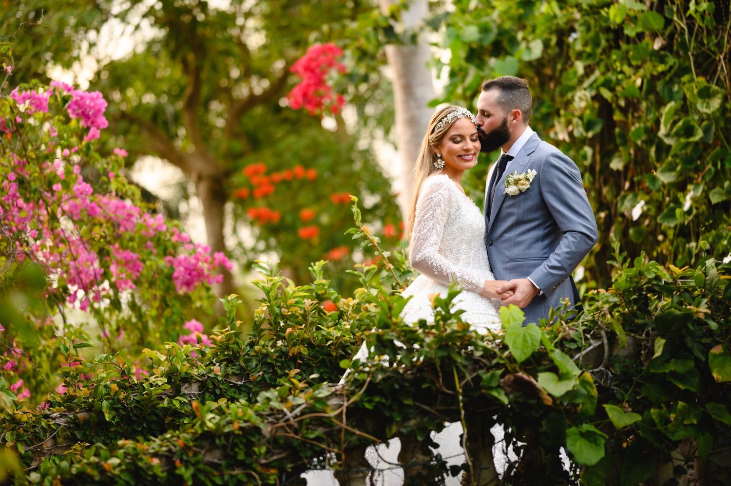 Bride and groom share a romantic moment surrounded by lush greenery and colorful flowers in a garden setting.