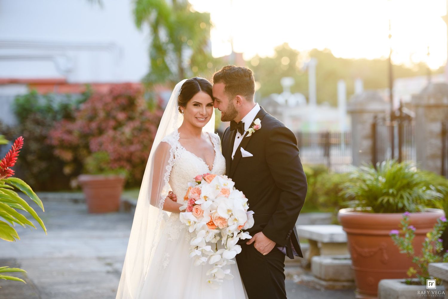 Smiling bride and groom pose together at sunset, bride carrying an elegant peach and white wedding bouquet.