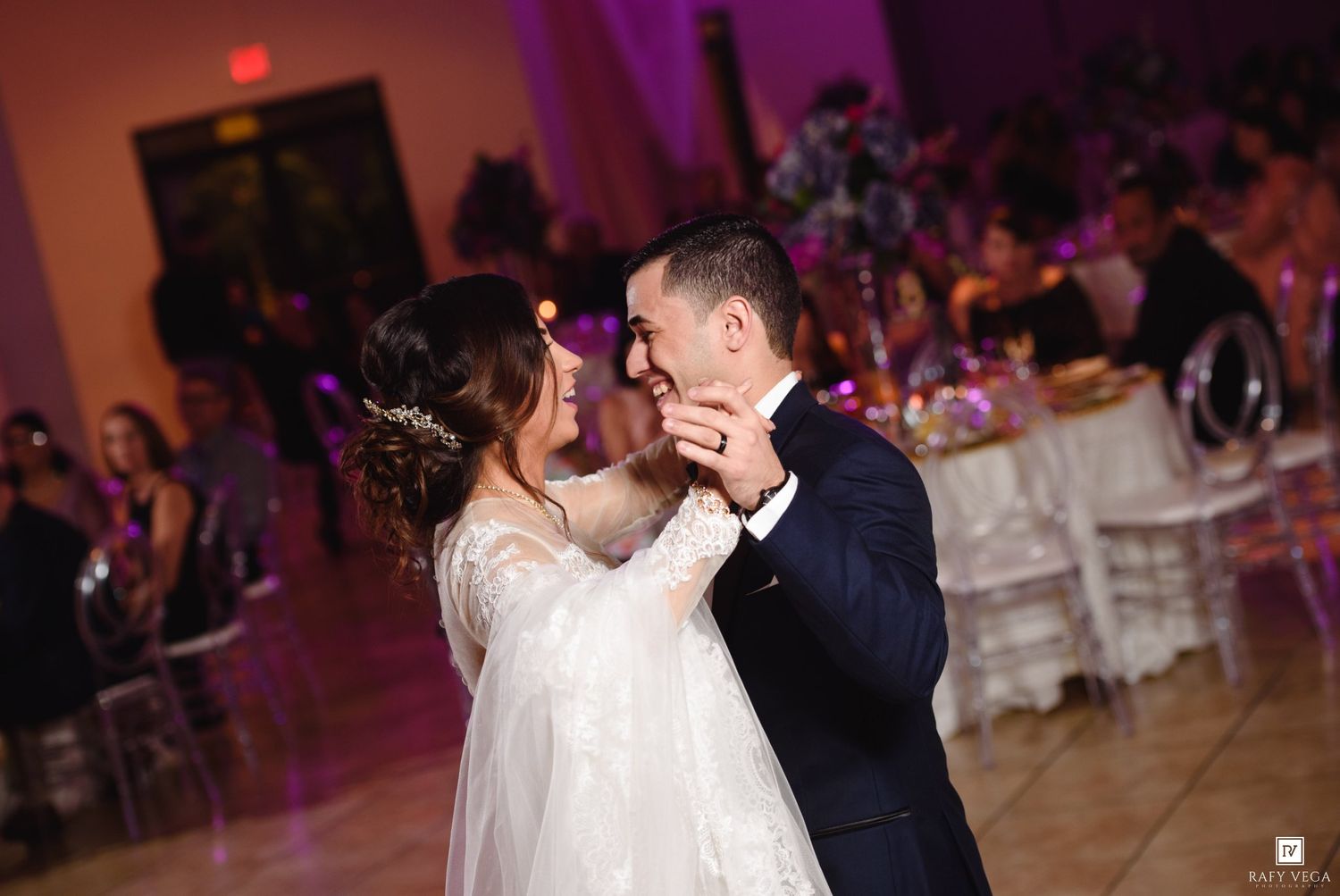 Bride and groom share their first dance at a romantic wedding reception with purple ambient lighting.