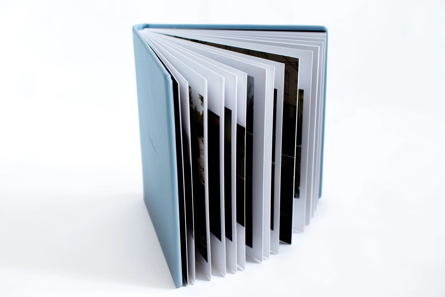 Light blue hardcover photo book standing open, displaying multiple pages with photographs on a white background.