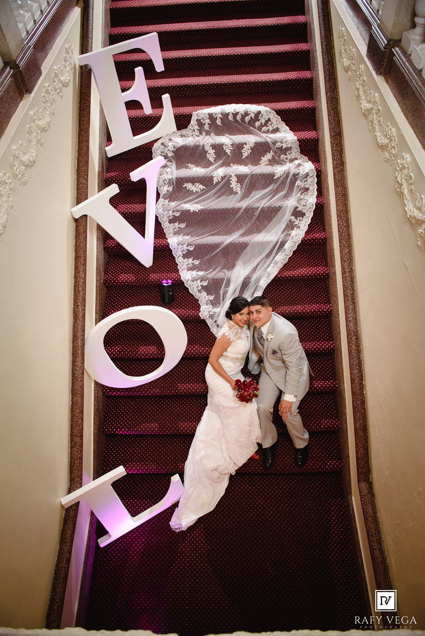 Aerial view of bride and groom on red carpeted staircase surrounded by large LOVE letters.