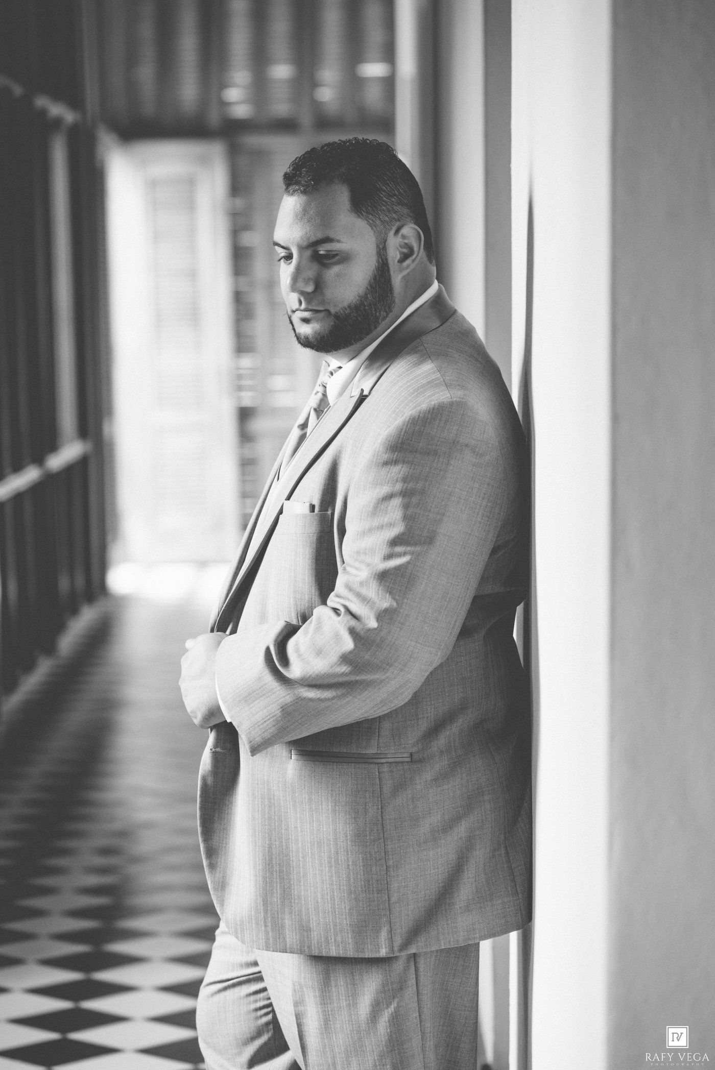 Black and white photo of a well-dressed man in a suit leaning against a column in an elegant hallway.