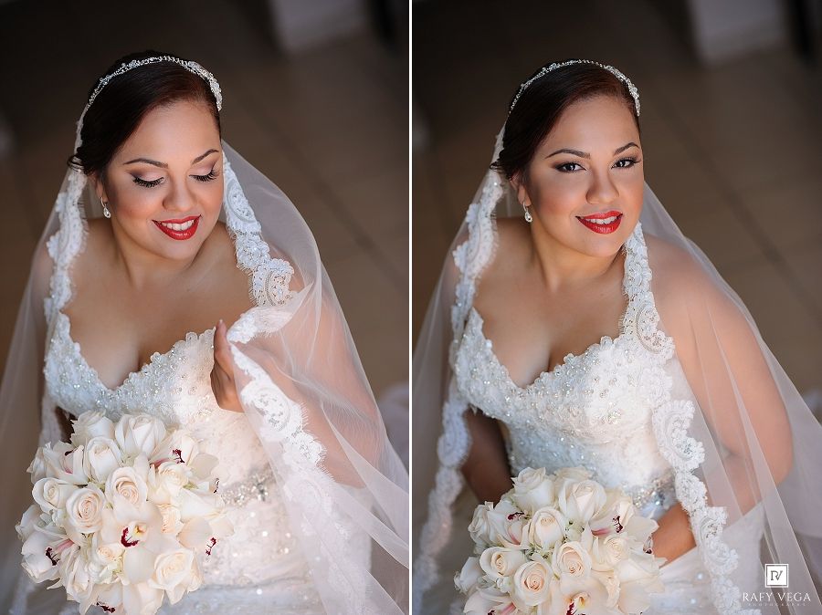 Elegant bride in lace wedding dress and veil holding white rose bouquet, smiling beautifully in a bridal portrait.