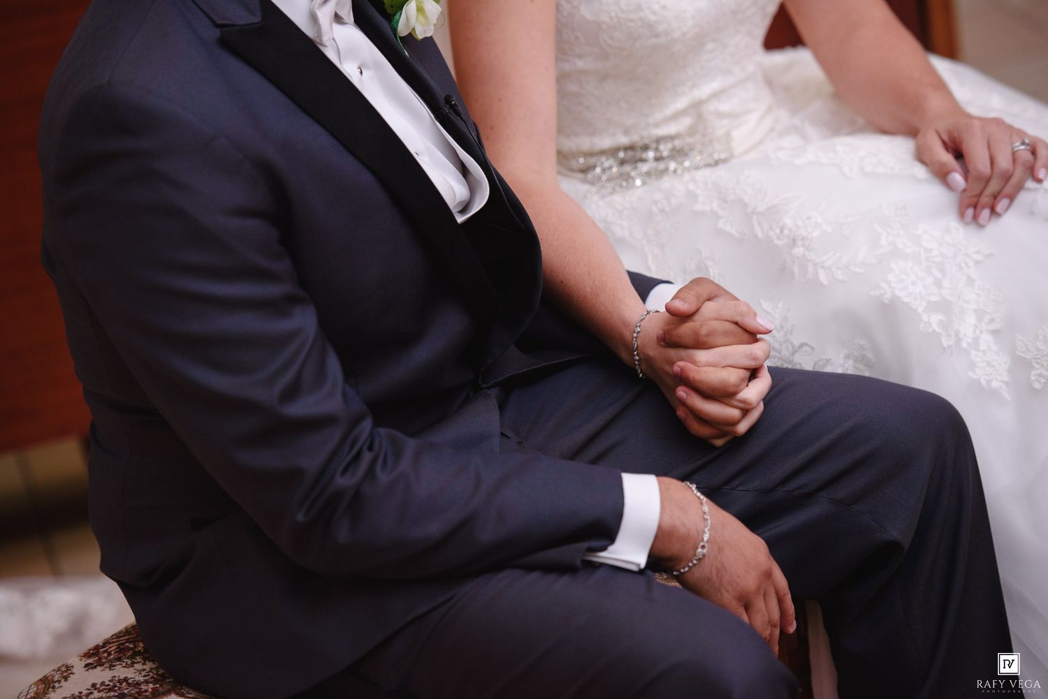 Bride and groom holding hands during wedding ceremony, wearing formal attire.
