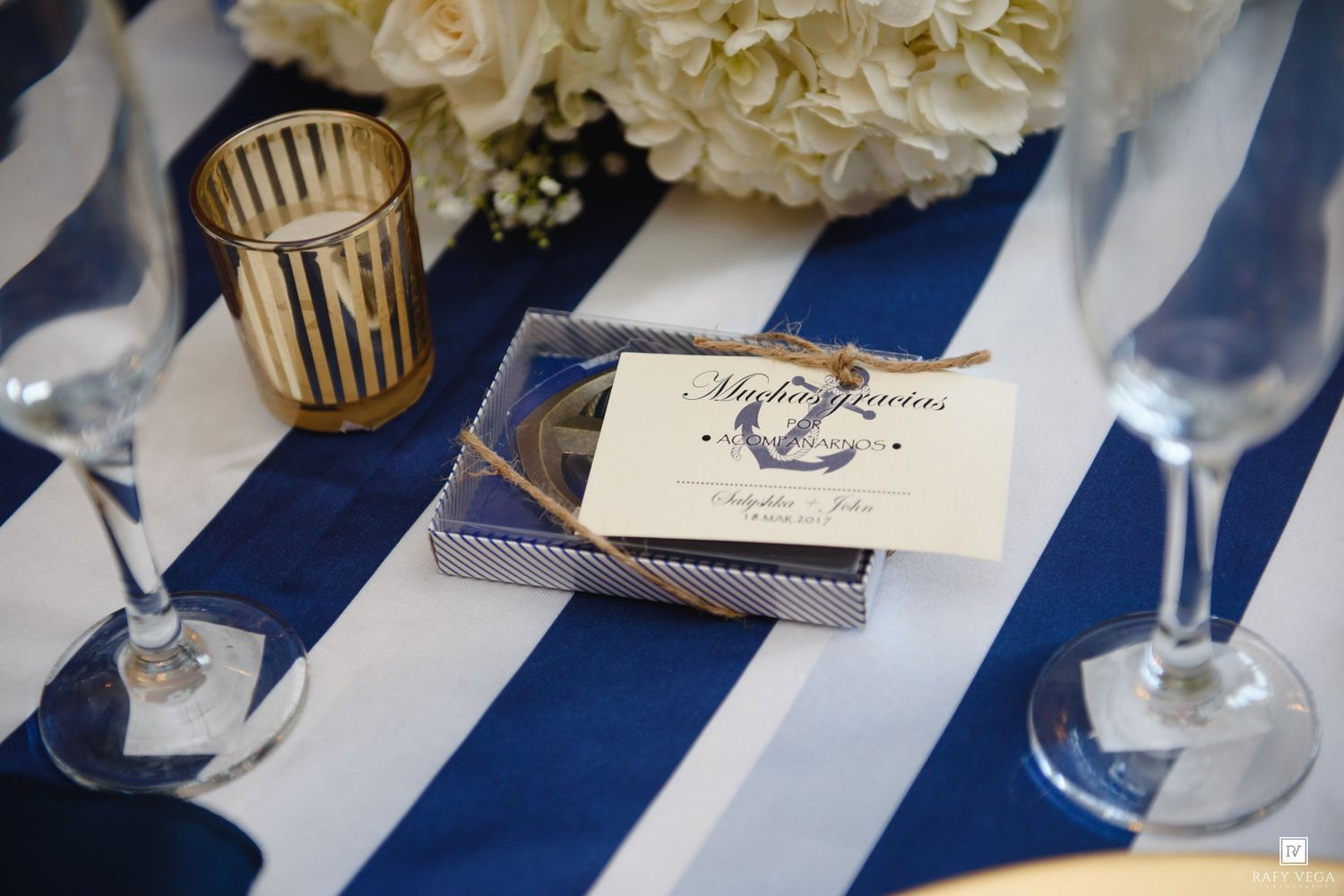 Navy striped tablecloth with nautical anchor wedding favor box, champagne glasses, and white floral centerpiece.