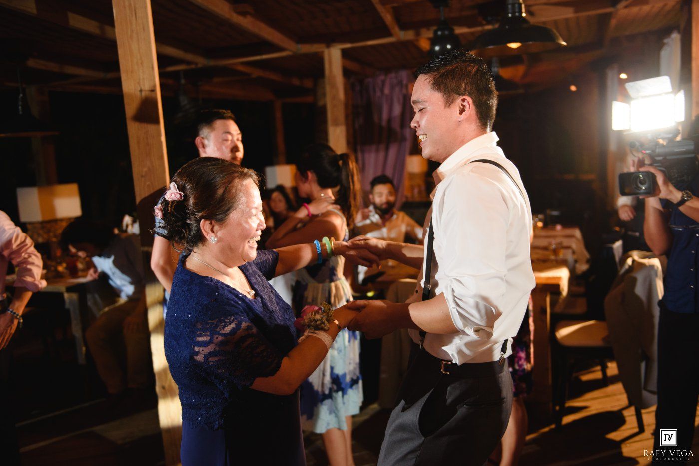 Groom shares a tender dance with his mother during a warm wedding reception in a rustic venue.