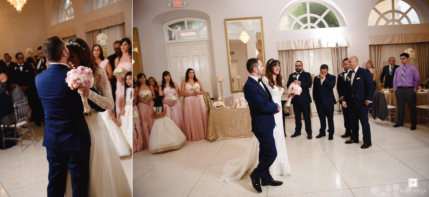 Bride and groom share first dance at elegant wedding reception with bridesmaids in pink dresses and guests watching.