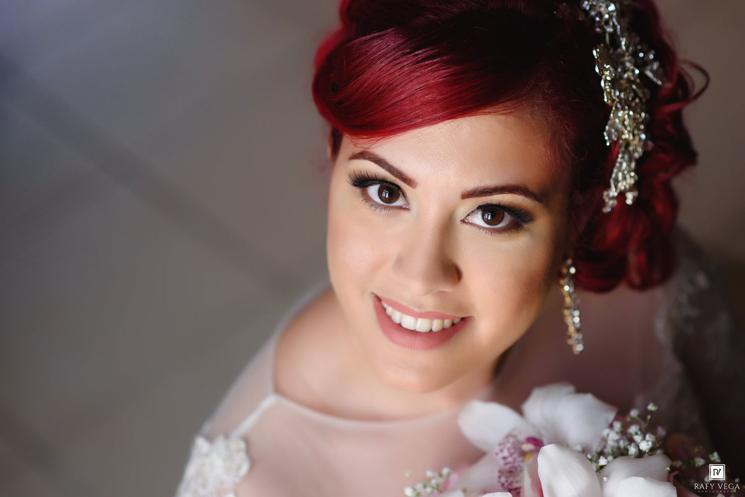 A smiling bride with vibrant red hair adorned with crystal hair accessories wearing a white wedding dress.