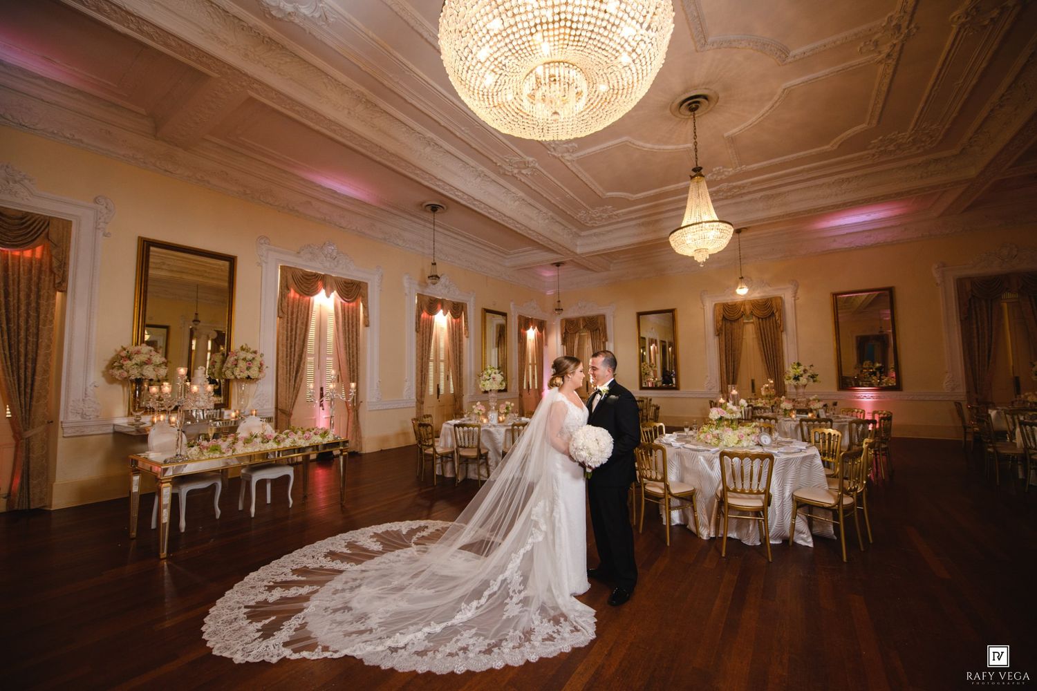 Bride and groom share a romantic moment in an elegant ballroom with crystal chandeliers and gold wedding reception decor.