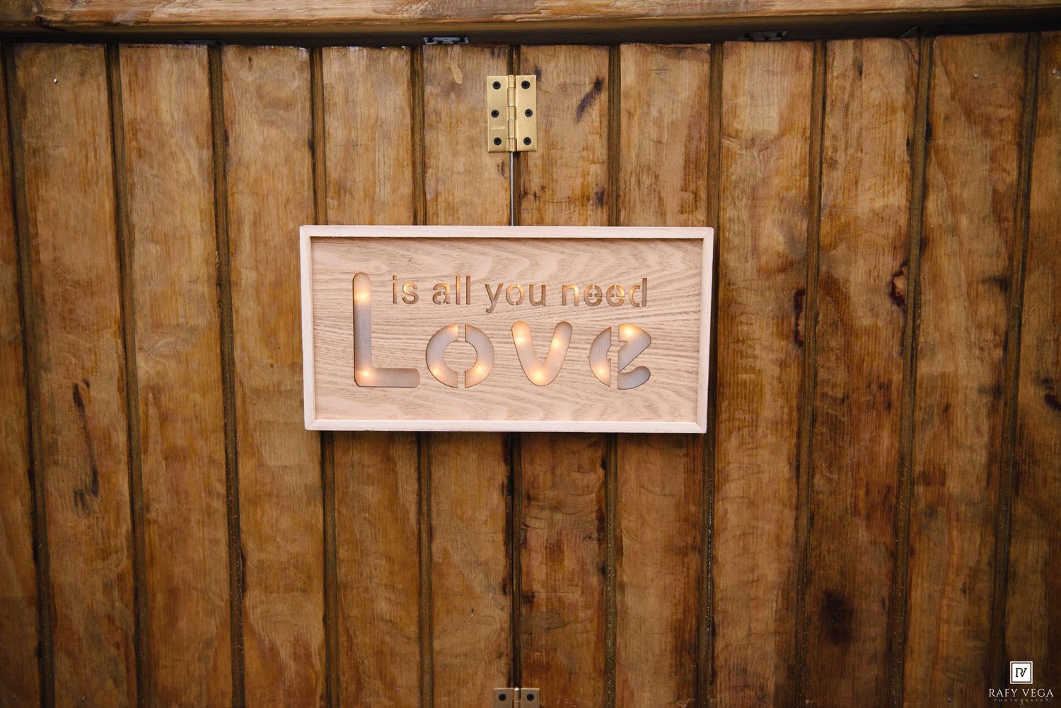 Wooden sign reading Love is all you need mounted on a rustic wood wall.