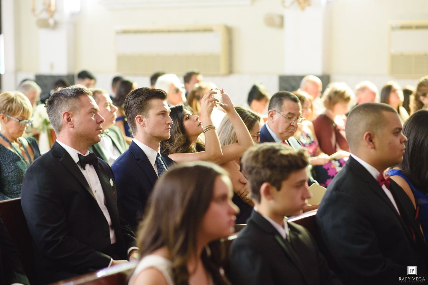 Wedding guests seated in elegant church pews during a ceremony, dressed in formal attire.