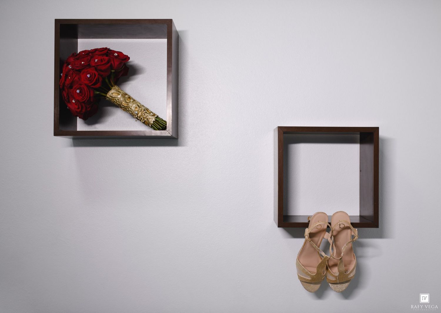 Two wall-mounted shadow box shelves display a red bridal bouquet with gold handle and nude strappy heels against a white wall.