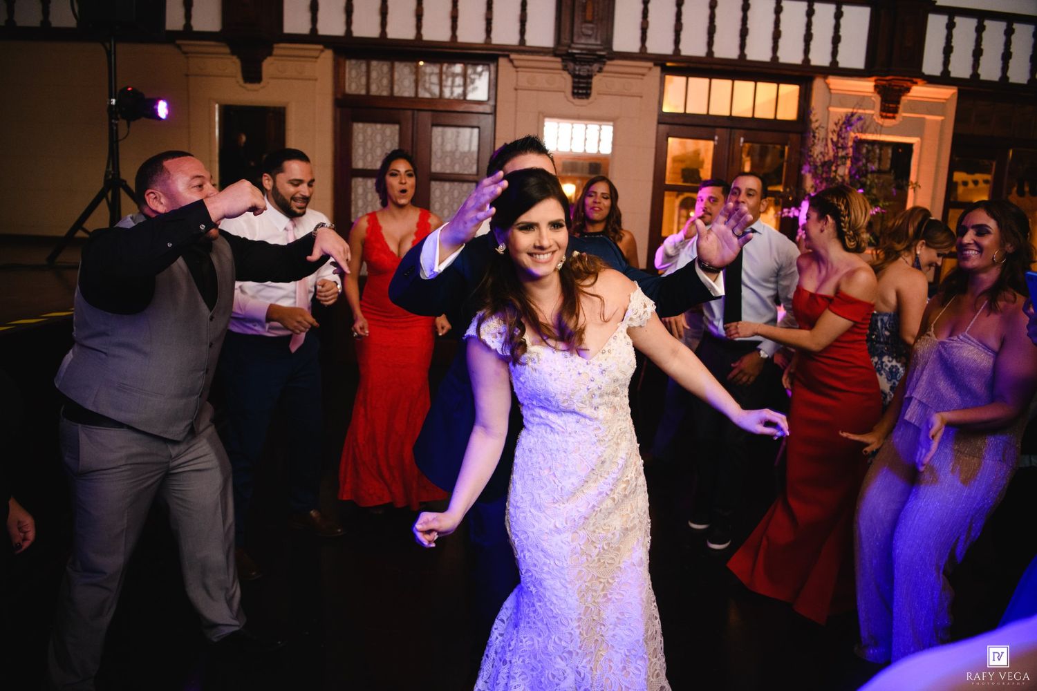 Bride in lace wedding gown dancing joyfully with guests at elegant wedding reception celebration.