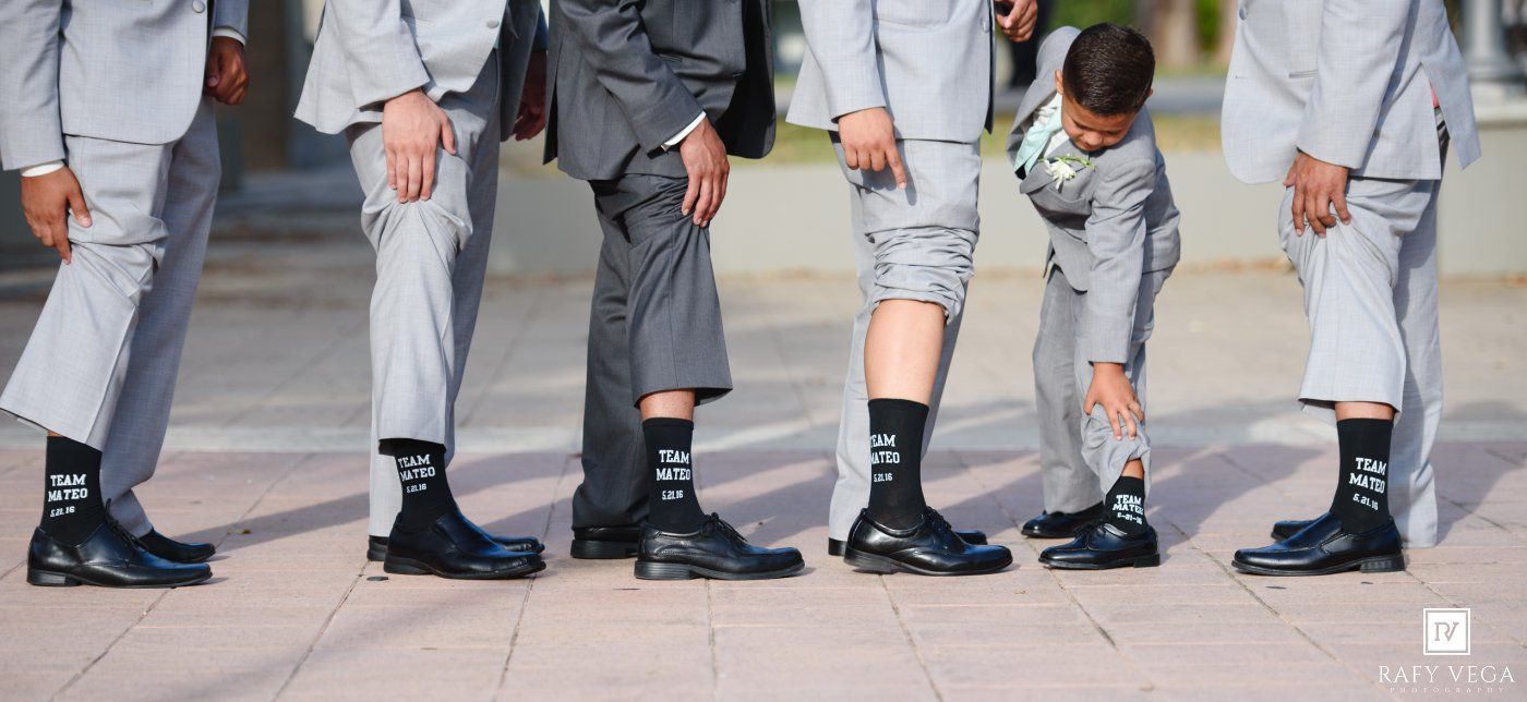 Groomsmen in gray suits showing off matching black socks with a young ring bearer.