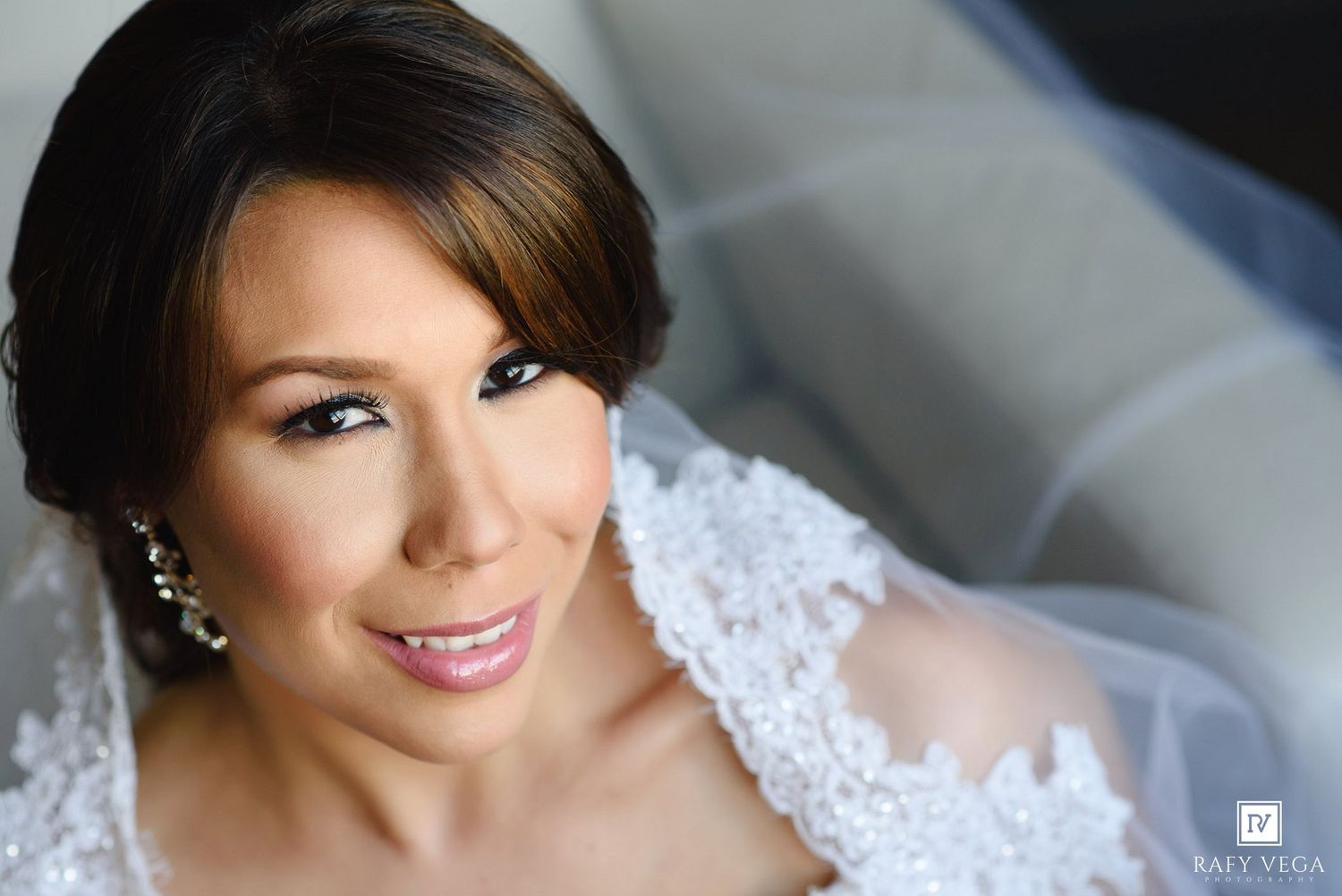 Close-up portrait of a beautiful bride in white lace wedding dress with veil and elegant jewelry.