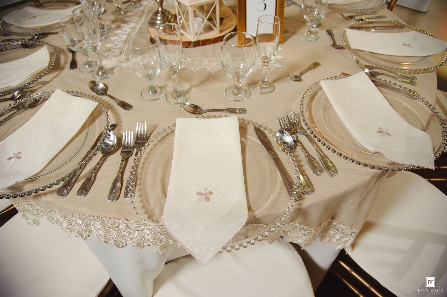 Elegant wedding reception table setting with silver-rimmed chargers, crystal glasses, and embroidered linen napkins.