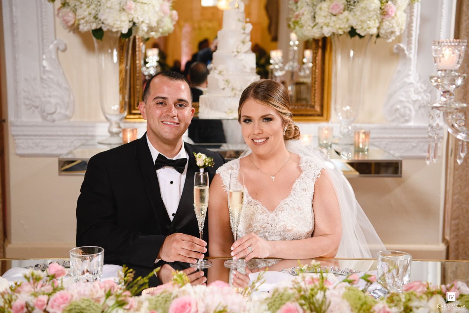 Bride and groom smiling and holding champagne glasses at elegant wedding reception with floral arrangements.