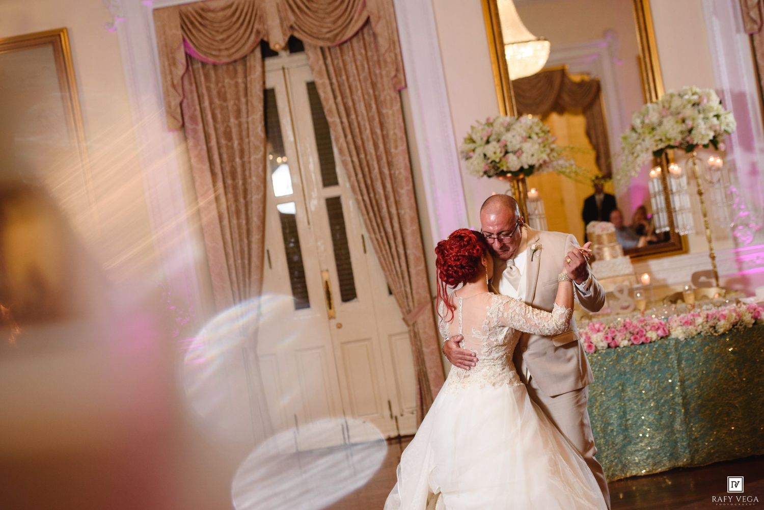 Bride and groom share their first dance in an elegant ballroom decorated with white floral arrangements.