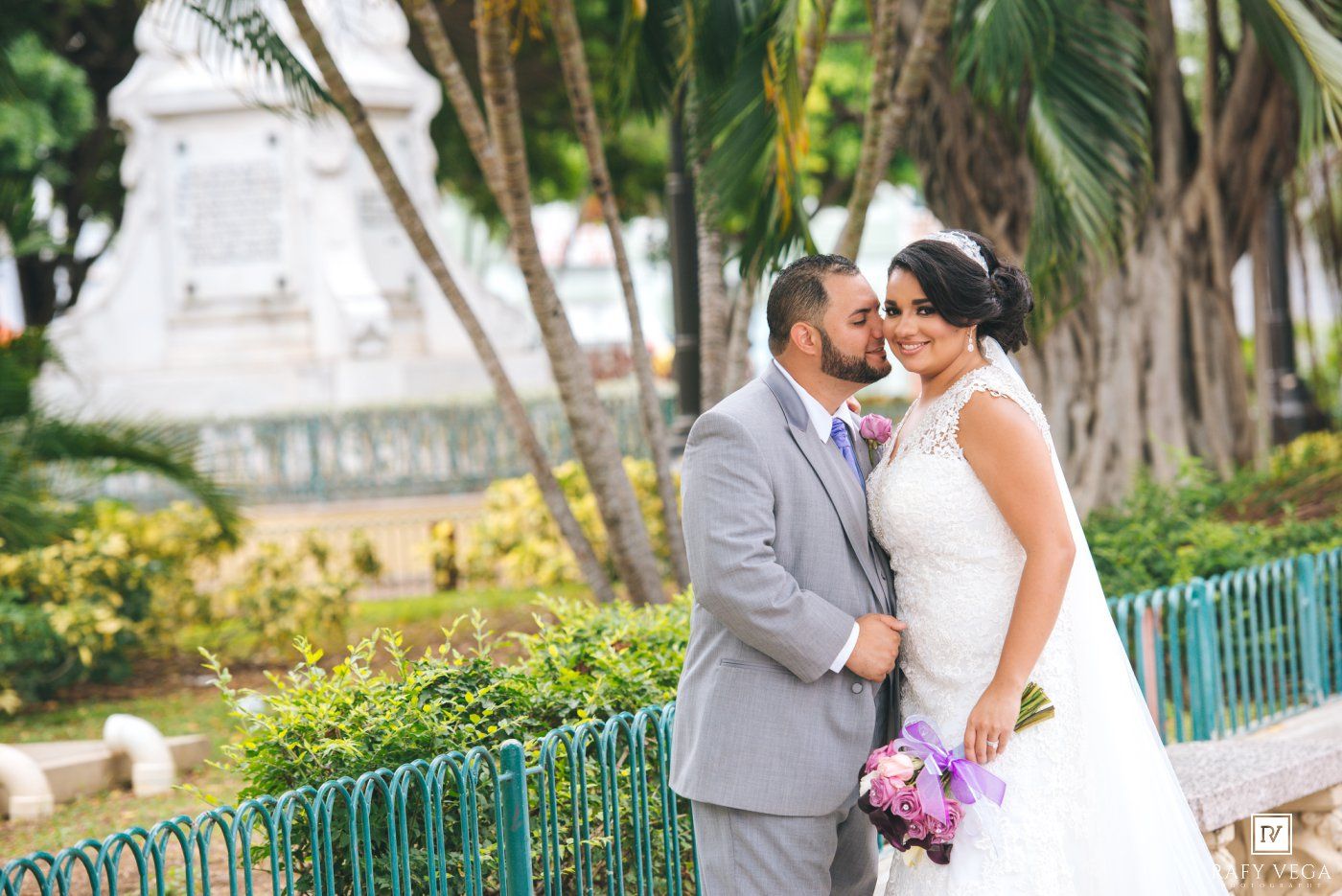 Bride and groom share a romantic moment in a lush garden, with the bride holding a purple bouquet.