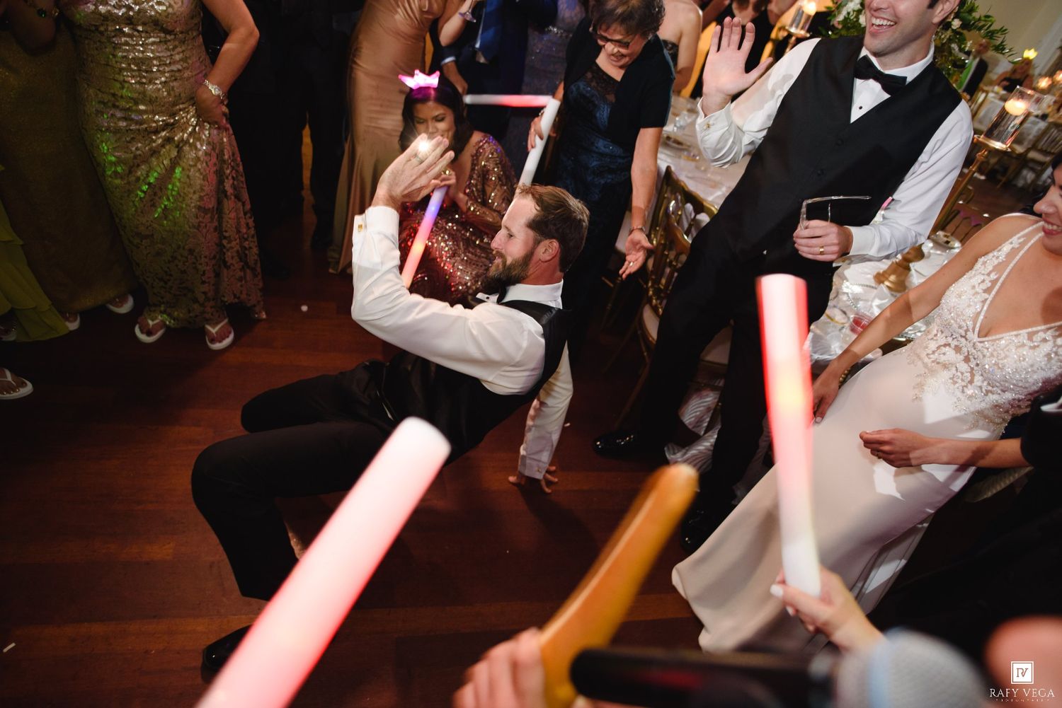 Guests dance with glowing light sabers at a lively wedding reception on a hardwood dance floor.