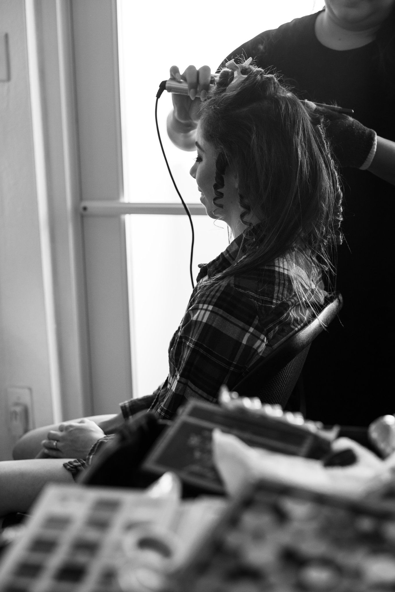 Black and white photo of a woman getting her hair styled with a curling iron at a salon.