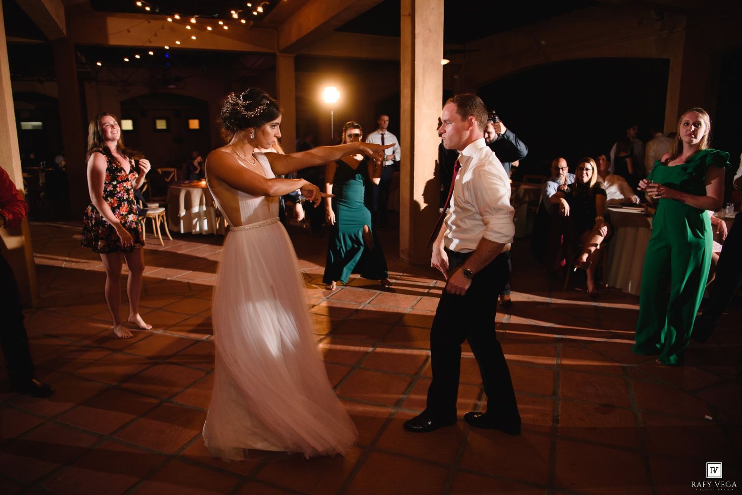 Bride and groom share a lively dance at their wedding reception while guests watch and celebrate in the background.