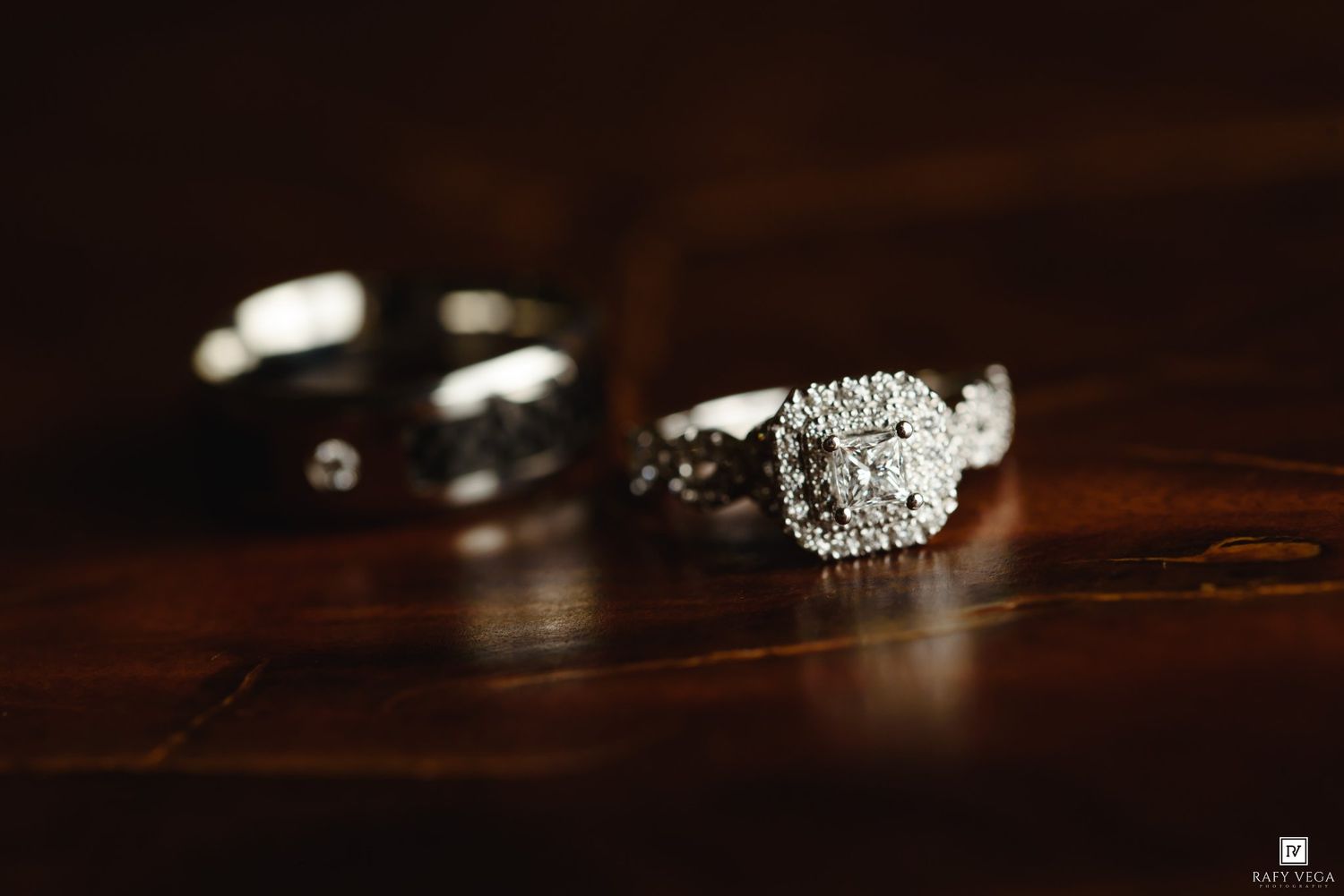 Close-up of diamond engagement ring and wedding band on dark wood surface.