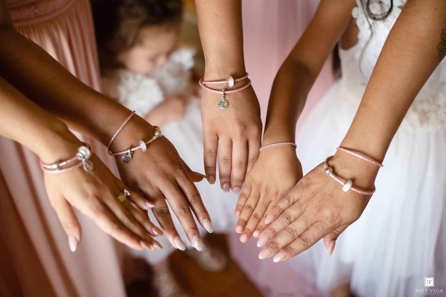 Bridesmaids and bride showing off matching rose gold charm bracelets and manicured nails in a wedding preparation photo.