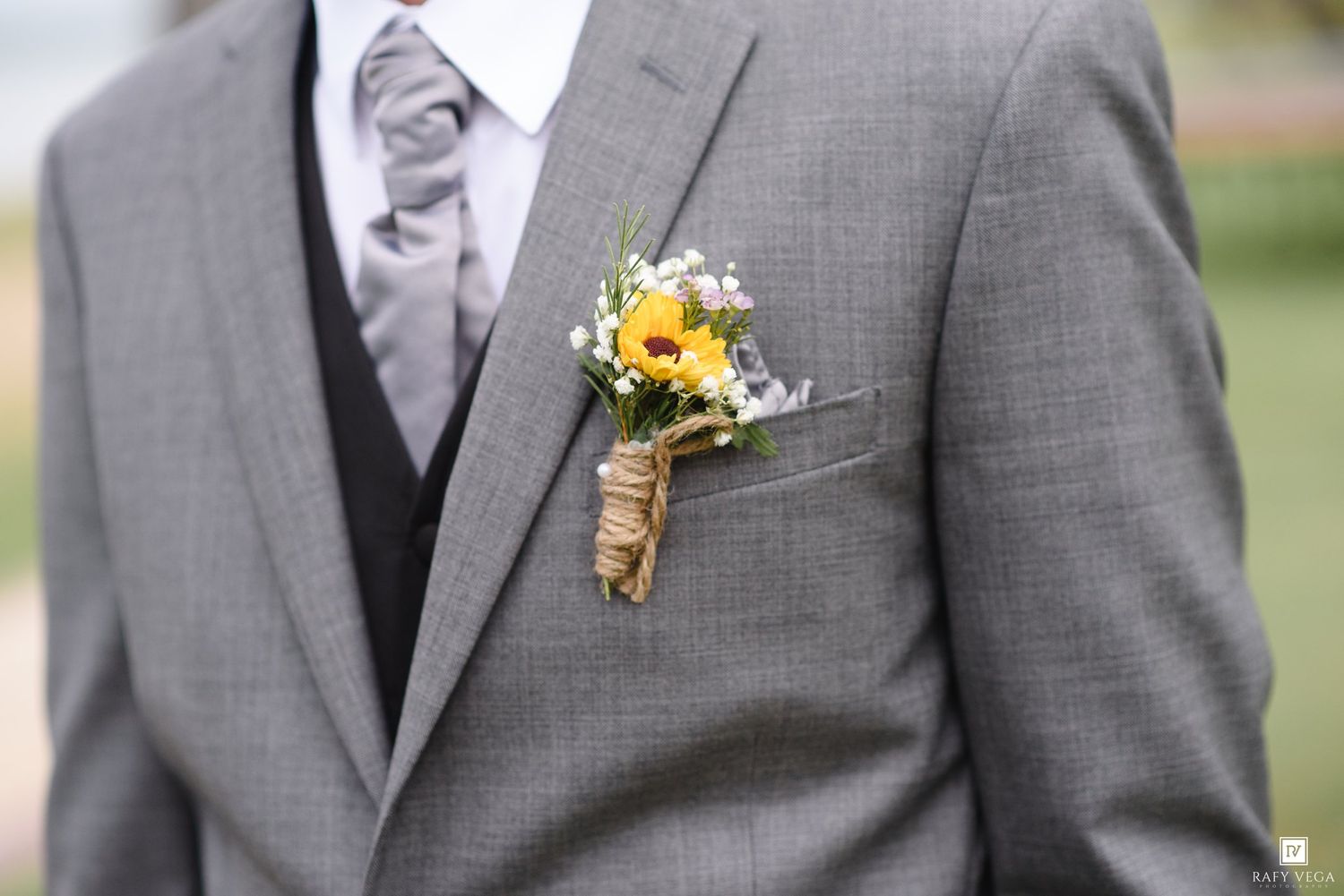Groom in gray suit with yellow sunflower and wildflower boutonniere wrapped in burlap twine.