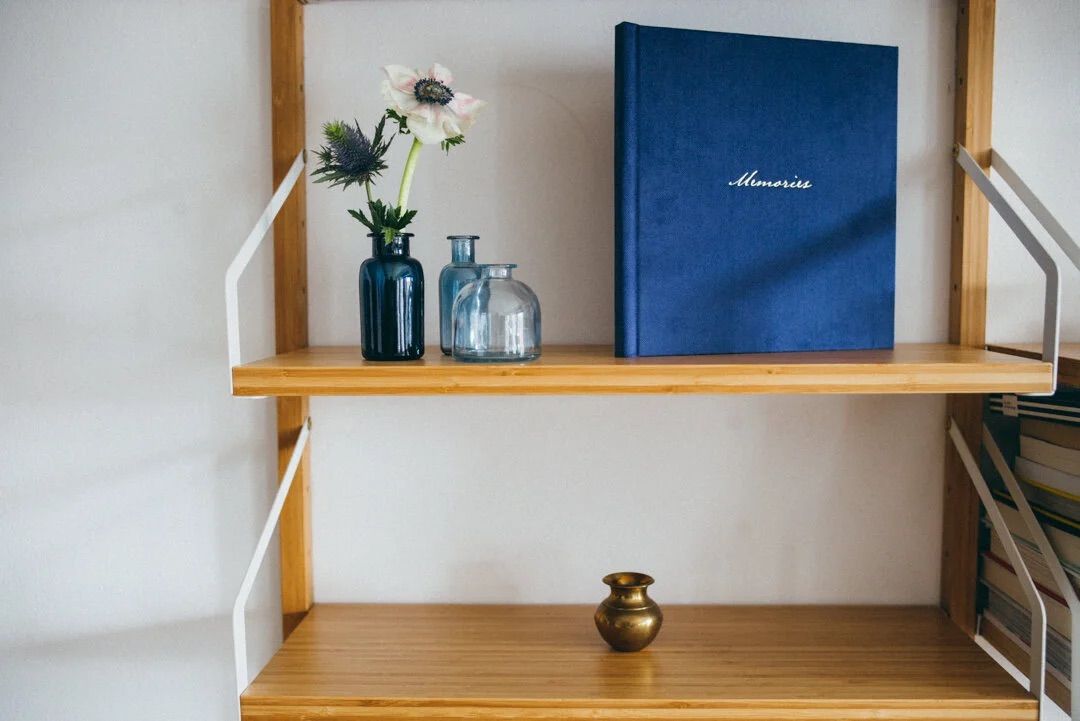 Wooden shelf with blue Memories book, glass vases with white flowers, and a small brass vase.