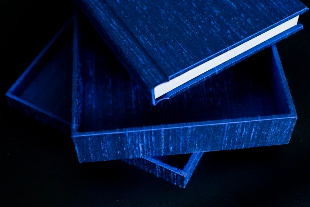 Two elegant royal blue textured gift boxes stacked on a dark background, with lid slightly open.