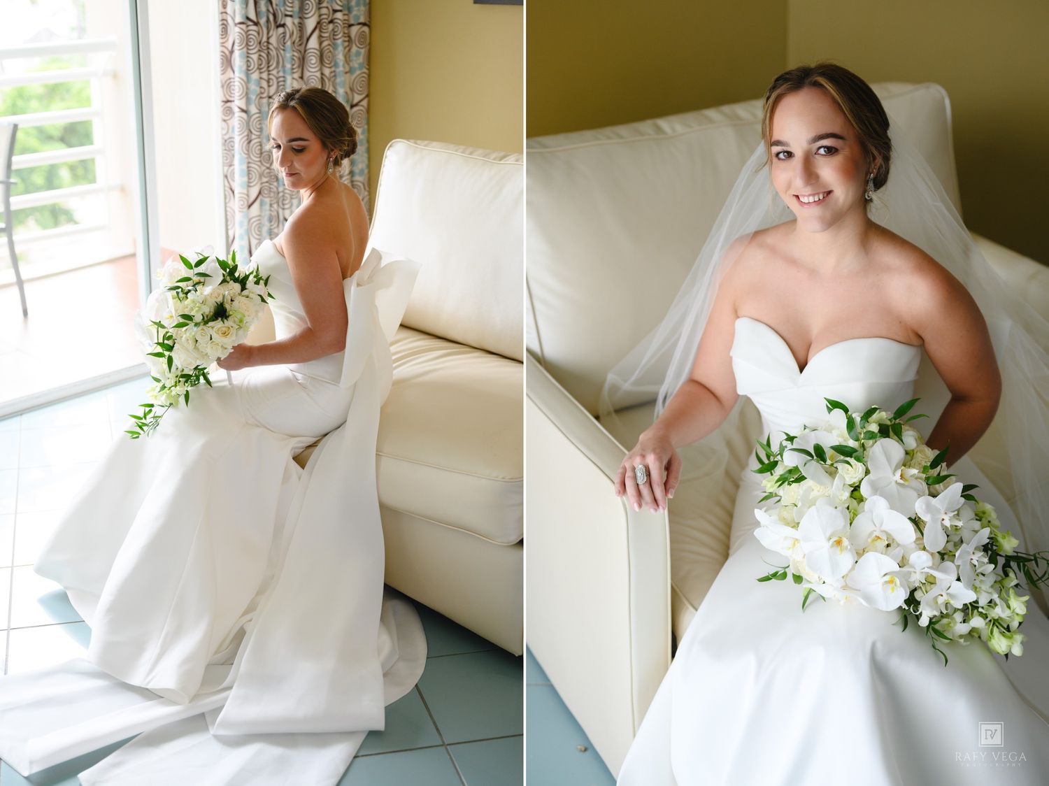 Elegant bride in strapless white gown holding white floral bouquet, seated by window in bright room.