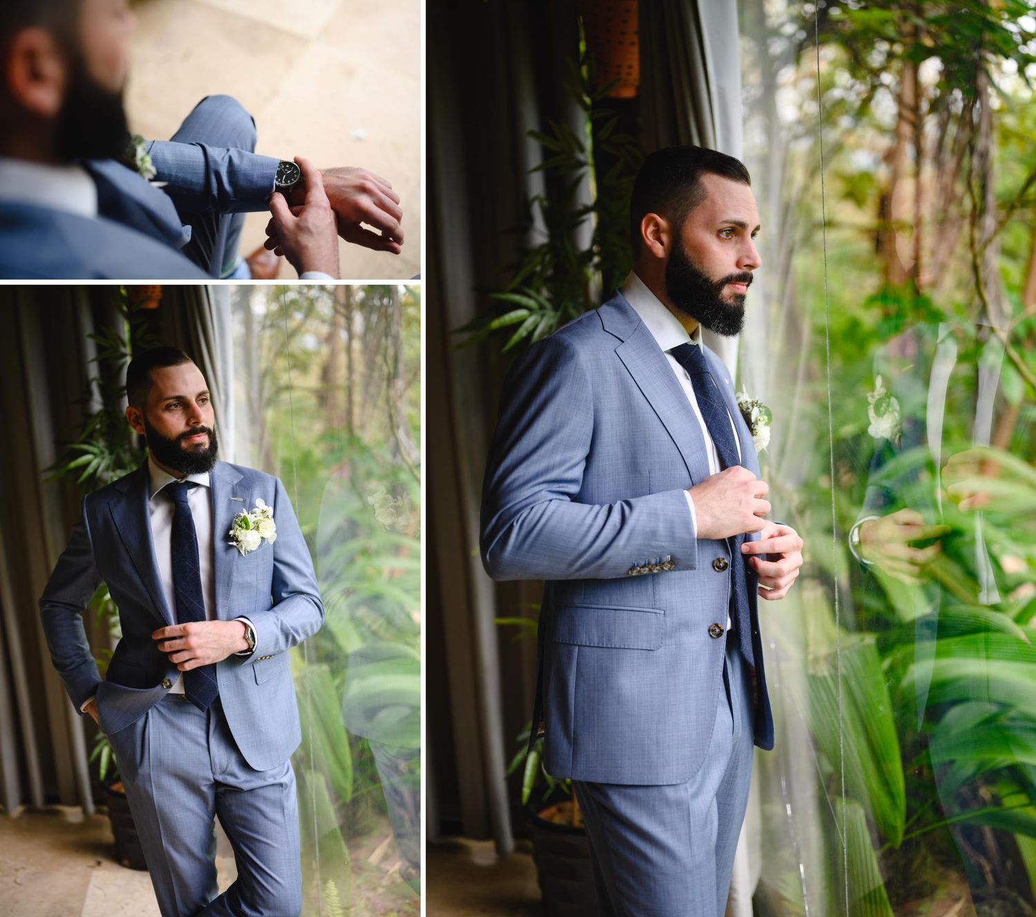 Groom in a blue suit adjusting his tie and boutonniere near a glass window surrounded by lush greenery.