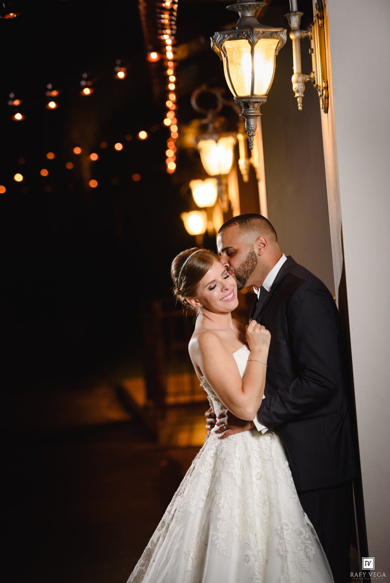 Bride and groom share a romantic kiss under glowing lanterns at night, bride wearing a stunning white ball gown.